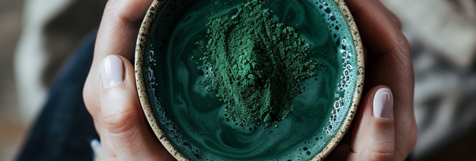 A woman’s hand holding a cup of green juice with green powder on top.