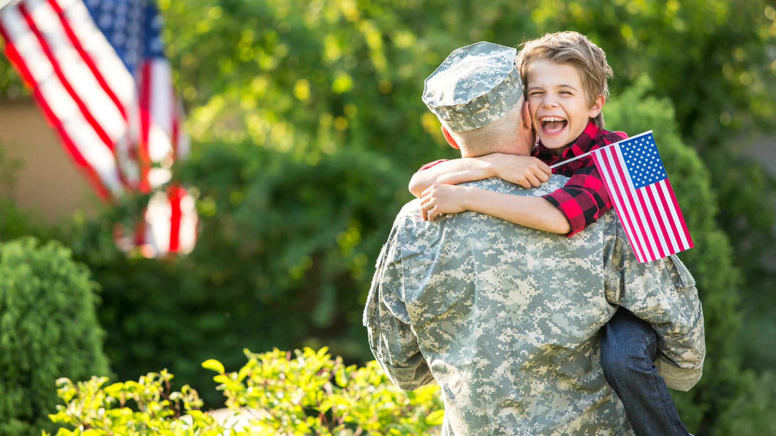 Heartwarming Military Welcome Home. Child smiling hugging his dad while holding the US flag